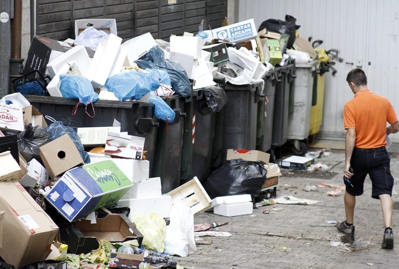 Un joven pasa ante contenedores desbordados de basura en una calle de Lugo. 