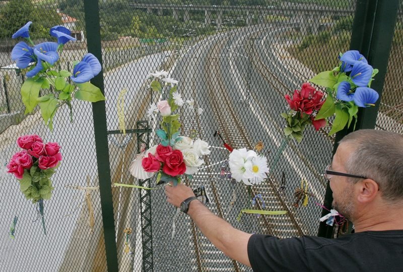 Un hombre deposita unas flores en la verja de la curva de A Grandeira, en Angrois. 