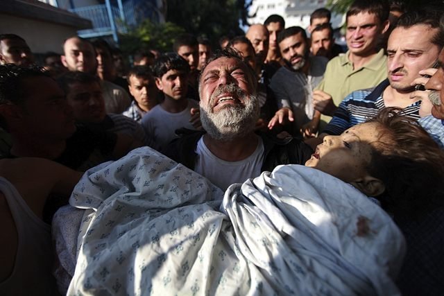Un palestino carga con el cuerpo de su hijo muerto en un bombardeo.