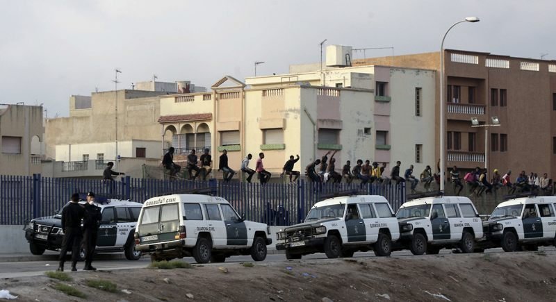 Un grupo de inmigrantes subidos a la valla de Melilla, bajo la atenta vigilancia de la Guardia Civil.