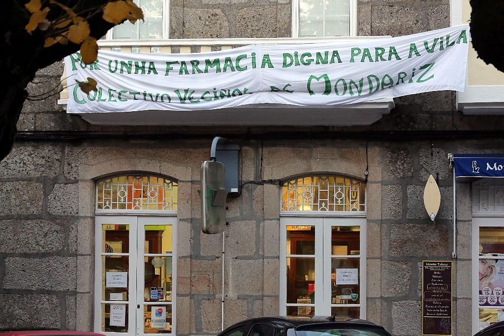 La farmacia Landeira en la Plaza de España de Mondariz coronada por una pancarta de protesta.