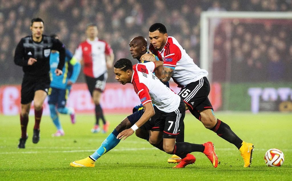 M'Bia, que marcó un gol mal anulado por fuera de juego, pelea por el balón con dos jugadores del Feyenoord.