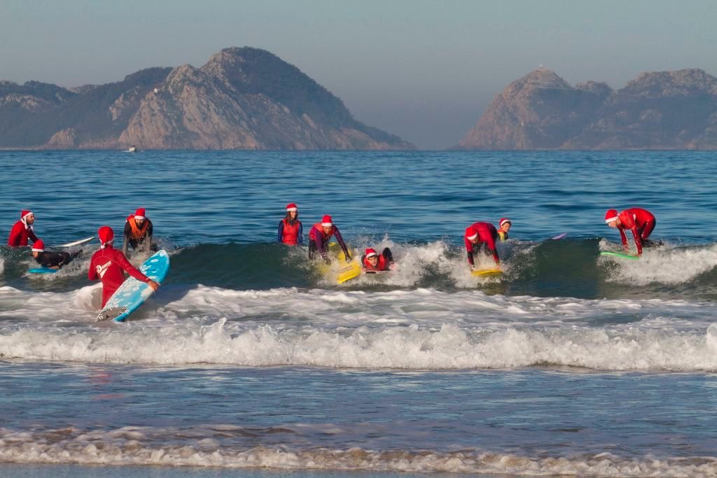 Un grupo de valientes surfistas disfrazados de Papá Noel coge una ola en la mañana de ayer en la playa de Patos.