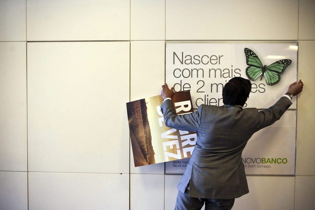 Un hombre coloca una cartel de la entidad Novobanco.