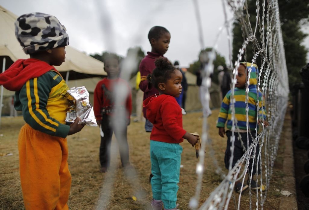 Varios niños, de familias que huyeron de los ataques xenófobos,  permanecen junto a una valla de un centro de refugiados de Cruz Roja 