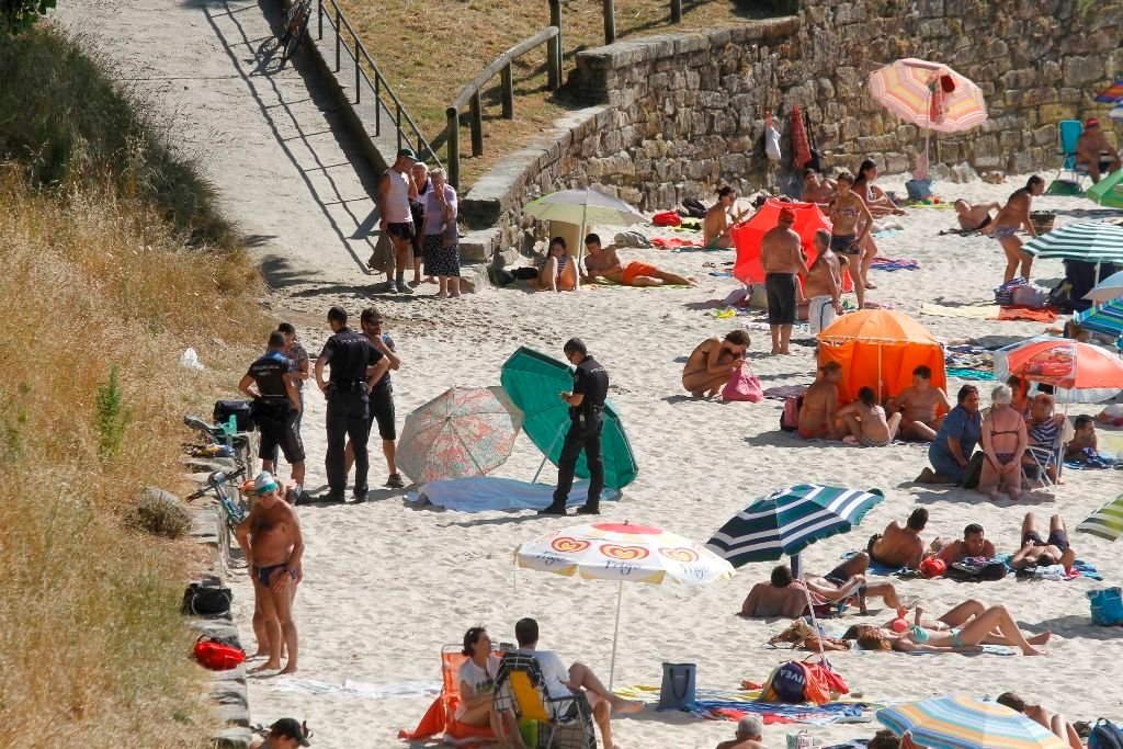 El cuerpo, envuelto en una tela, rodeado de policías y de bañistas en la playa de La Fuente. // Lanfoco