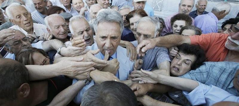 Un empleado del Banco Nacional de Grecia (c) es asediado por un grupo de pensionistas mientras distribuye números para ser atendidos a las puertas de una sucursal bancaria en Atenas
