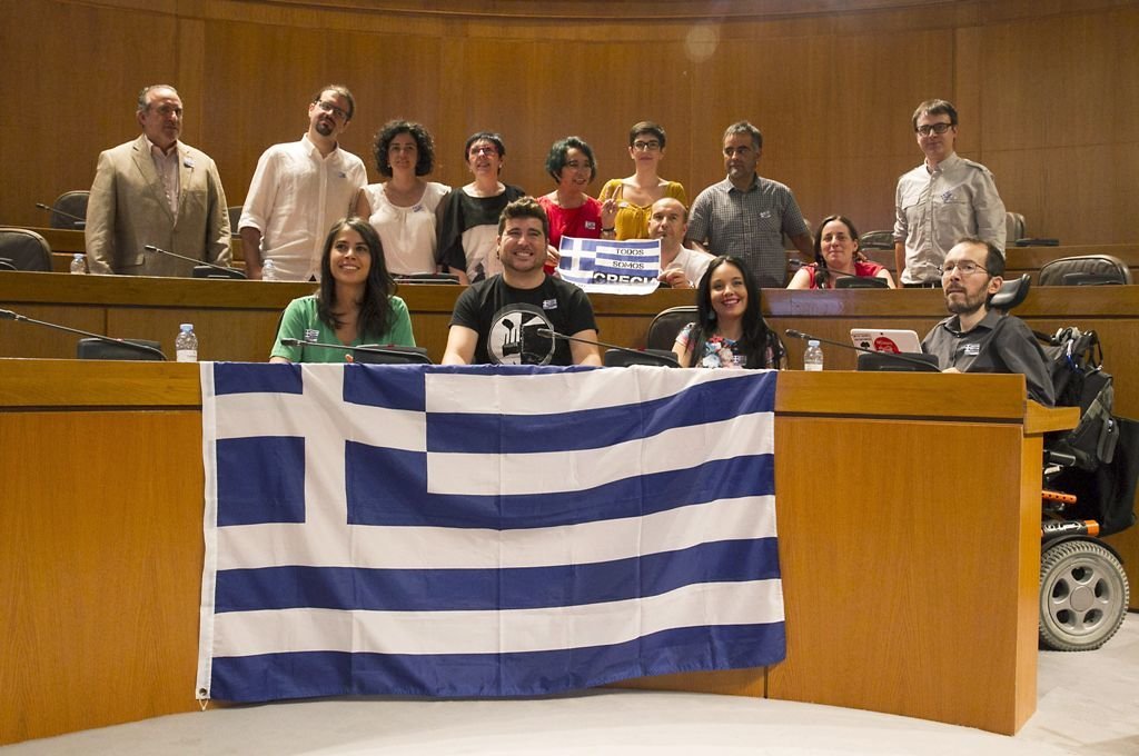 Los diputados de Podemos en Aragón muestran su apoyo con una bandera griega.