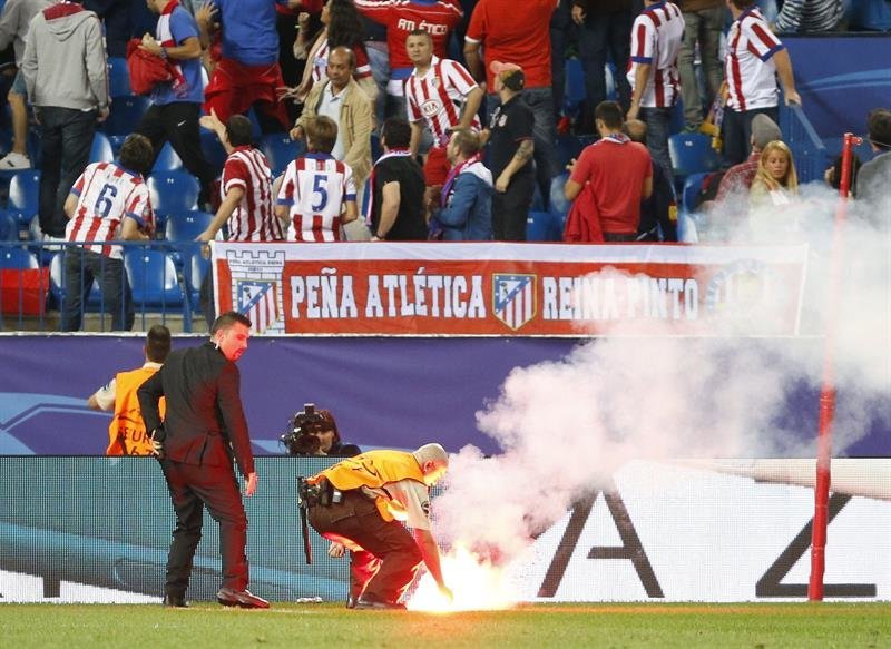 Operarios retiran una bengala del terreno de juego durante el partido entre Atlético de Madrid y Benfica en el estadio Vicente Calderón