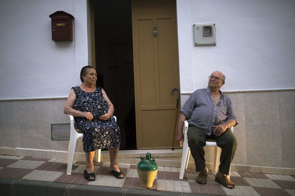 Dos personas mayores tratan de miigar el calor saliendo a la puerta de sus casa al atardecer.