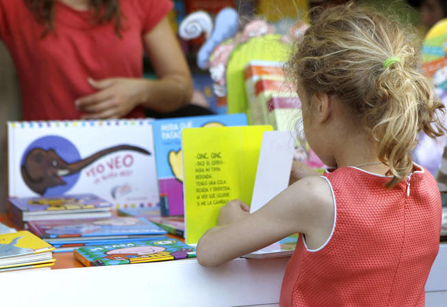 Una niña observa y selecciona libros de una biblioteca en un centro educativo.