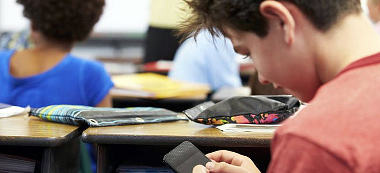 Un niño se dispone a consultar su teléfono móvil mientras se encuentra en clase.