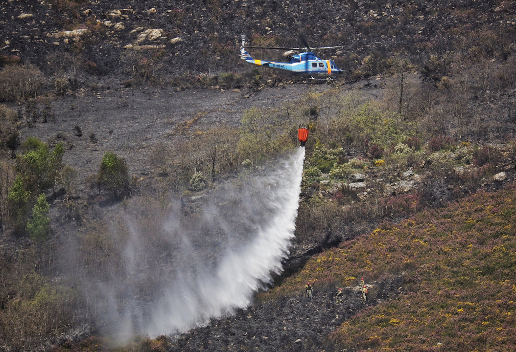 Un helicóptero arroja su carga de agua para refrescar la zona quemada en Quiroga, Lugo.