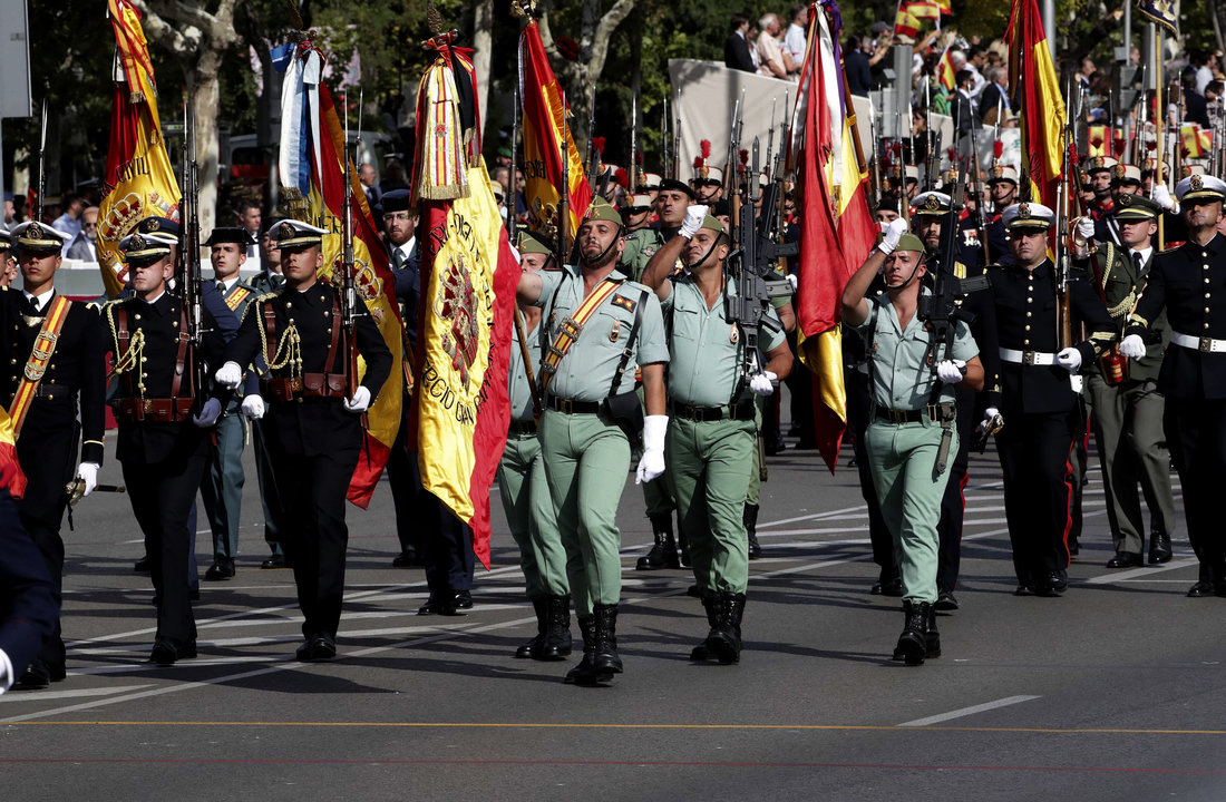 Las banderas de las unidades participantes en la parada militar desfilan rodeadas de enseñas nacionales en el Paseo de la Castellana.