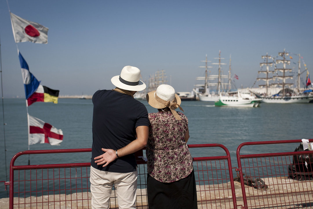 Una pareja de jubilados observa unos grandes veleros en el puerto de Cádiz.