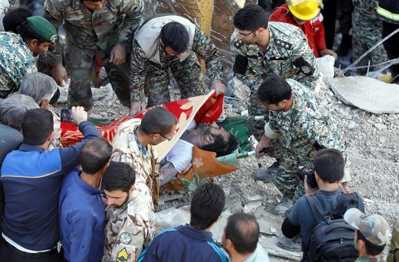 Miembros de la Media Luna Roja de Irán y los servicios de rescate protegen el cuerpo de una víctima entre los escombros de un edificio de Pole-Zahab, en la provincia de Kermanshah, Irán