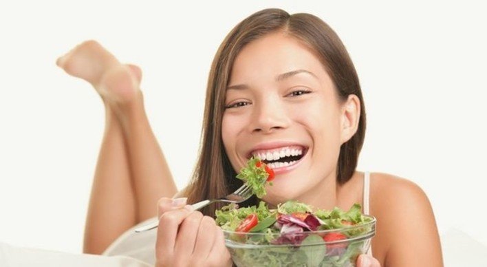 Una mujer sonríe mientras come una ensalada.