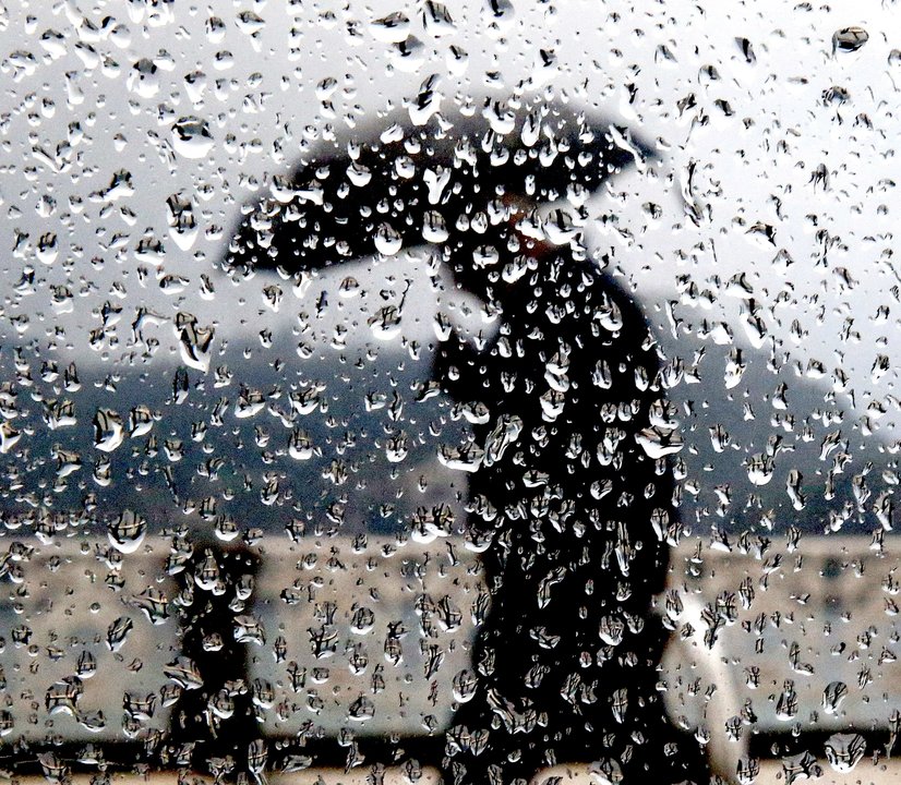 Personas caminando por la calle en un día de lluvia, vistas a través de un cristal.