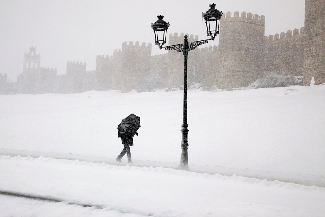 Una persona pasea ante las inmediaciones de las murallas de Ávila bajo una intensa nevada.
