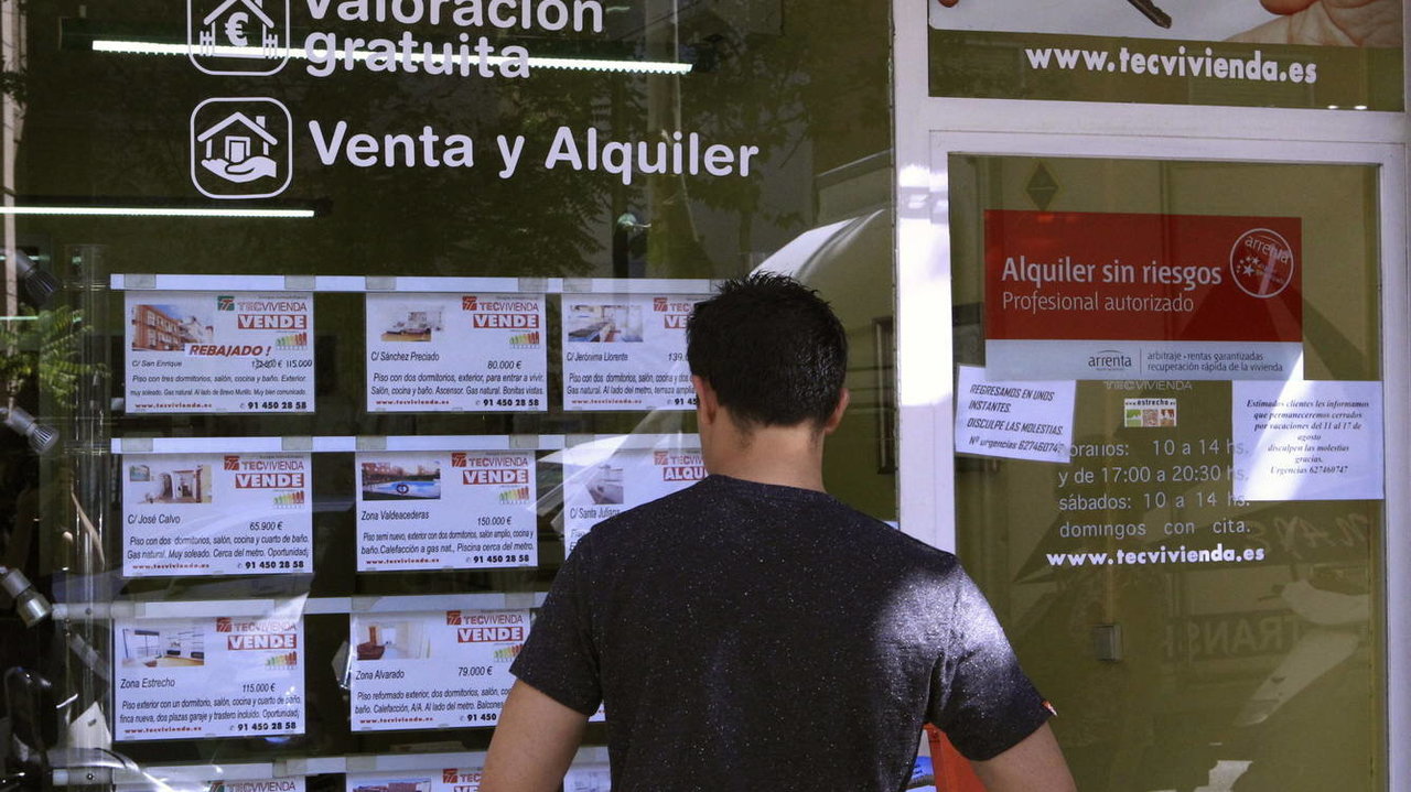 Un joven observa los carteles de ofertas de pisos de venta y alquiler en una inmobiliaria.