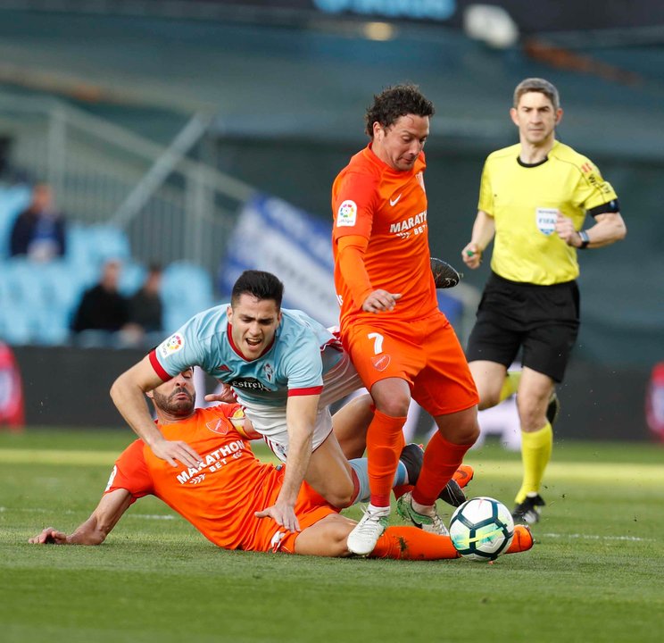 El céltico Maxi Gómez cae entre los malacitanos Lacen e Iturra durante el partido disputado ayer en el estadio de Balaídos.