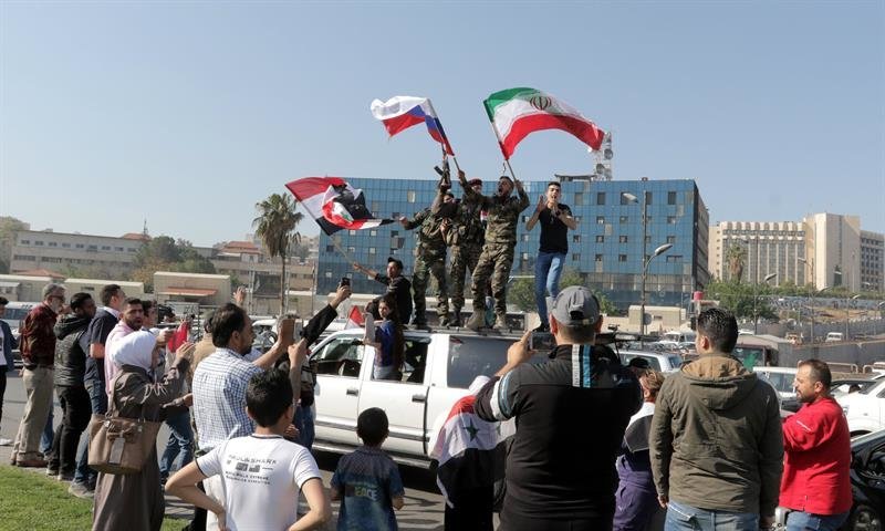 Soldados sirios ondean banderas nacionales junto con banderas iraníes y rusas
