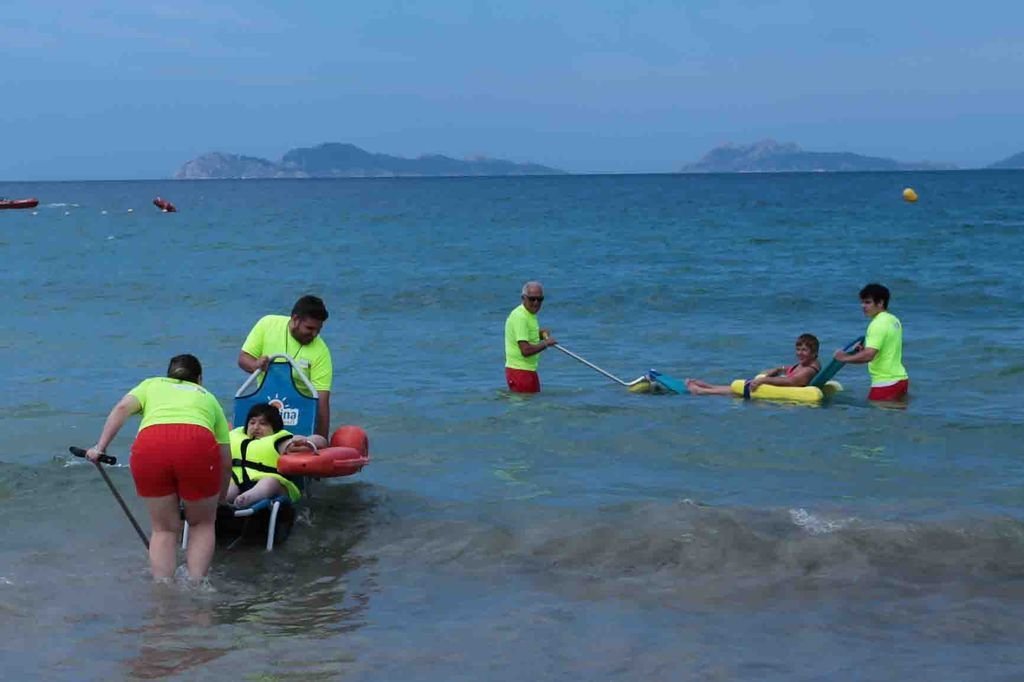 Usuarios de las sillas y el personal del puesto de socorro prueban las sillas adaptadas en el mar.