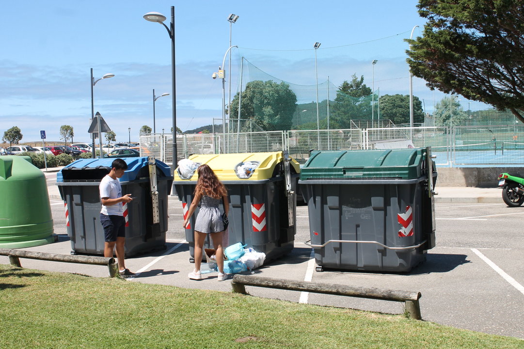 Dos jóvenes depositan la basura en el suelo ante la imposibilidad de meterla en el contenedor.