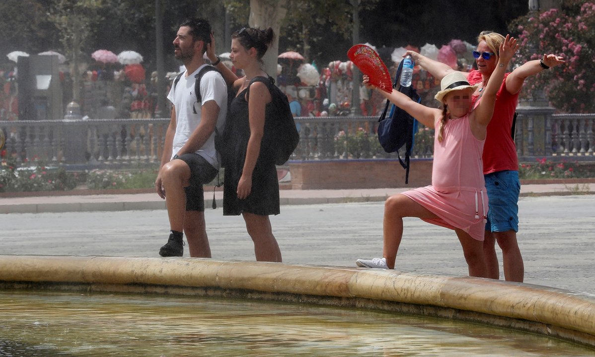 Varios turistas intentaban mitigar el calor en Sevilla refrescándose junto a una fuente pública.
