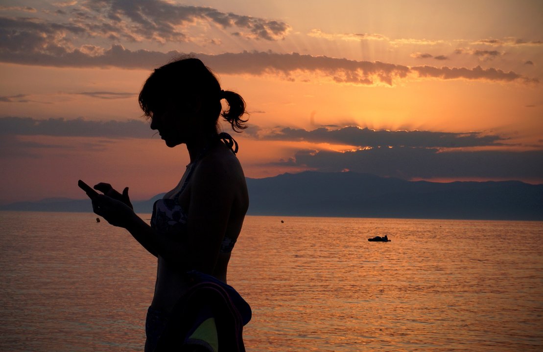 Una joven consulta su teléfono móvil mientras se encuentra en la playa.
