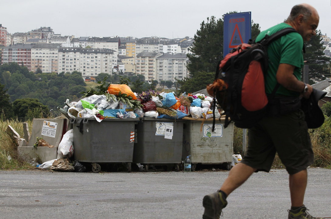 Un peregrino pasa ante unos contenedores rebosantes de basura, en Lugo.