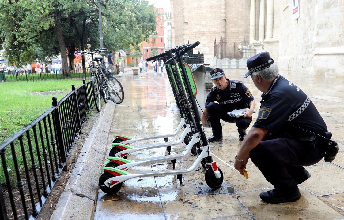 Dos agentes retiran patinetes eléctricos de alquiler en una calle de Valencia.