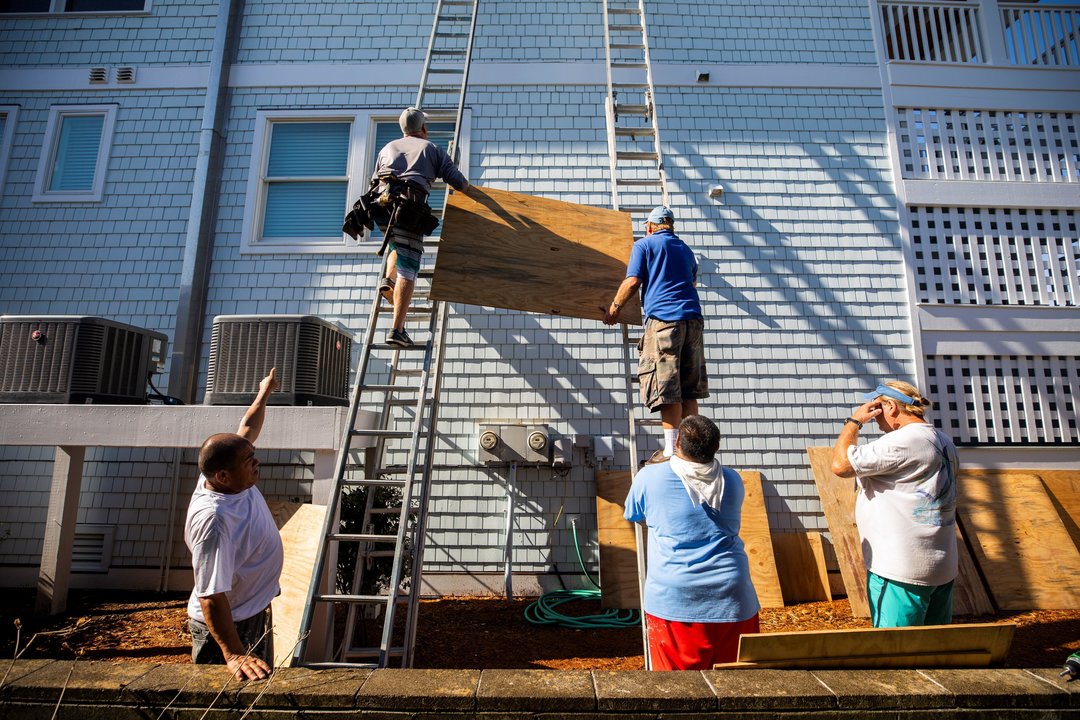 Dos hombres colocan planchas de madera sobre las ventanas de una vivienda en Carolina del Norte.