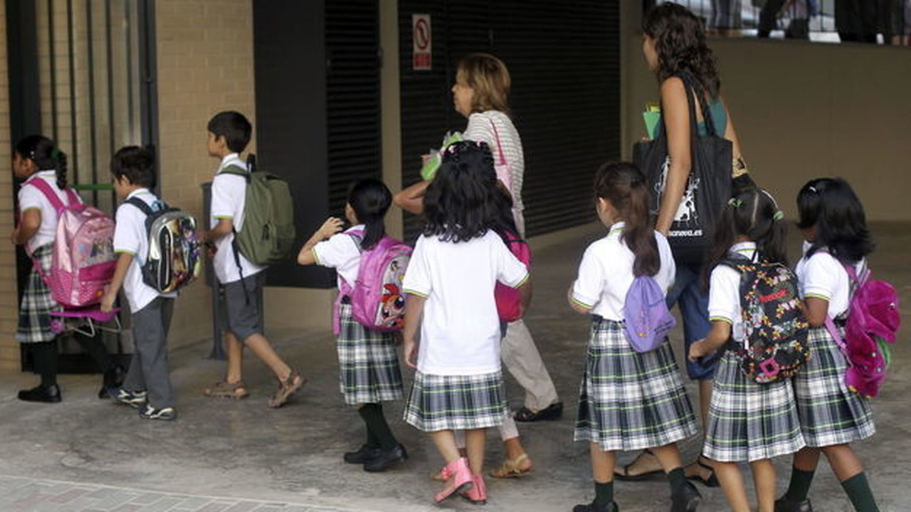 Un grupo de niñas con falda en el uniforme escolar entran en clase acompañadas de dos madres.