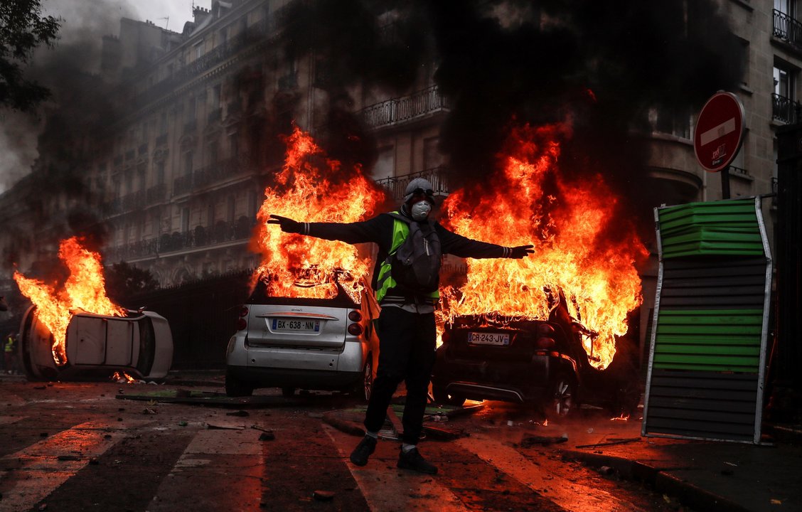 Un manifestante se deja retratar ante tres vehículos en llamas en una calle del centro de París.