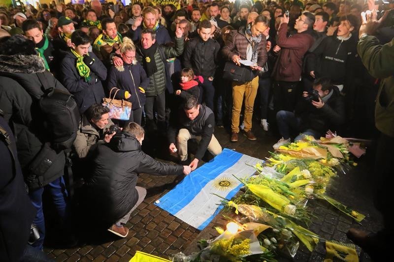 Dos hombres colocan la bandera nacional de Argentina sobre una ofrenda florar en conmemoración al jugador argentino de fútbol Emiliano Sala