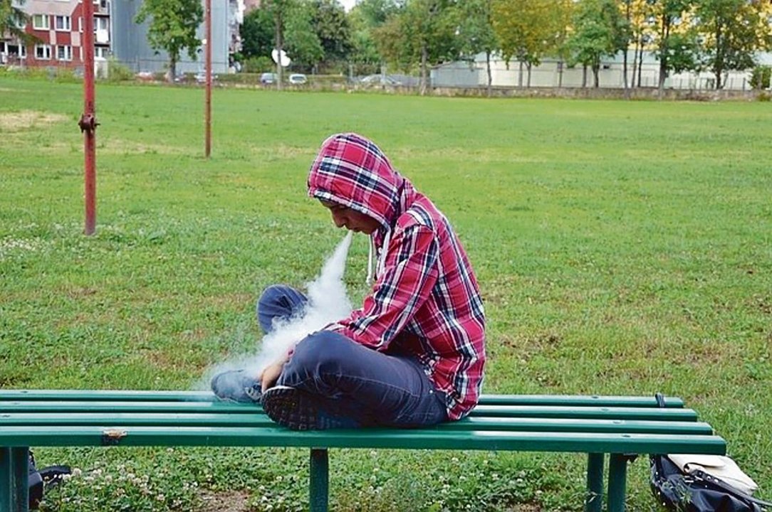 Un joven fumando en un banco de un parque en Oviedo.