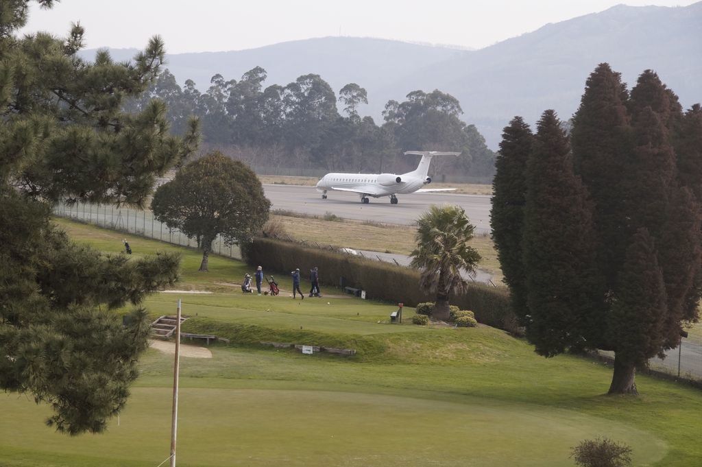 Jugadores del campo de golf del Aero Club, en plena acción con un avión despegando al lado.