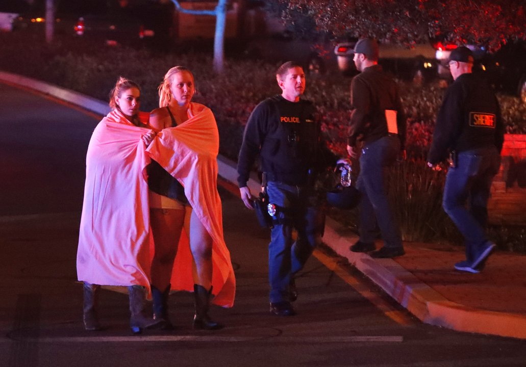 Dos mujeres envueltas en una sábana abandonan el área del tiroteo cerca del bar Borderline.