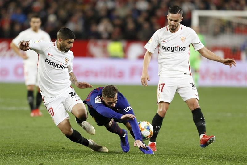 El centrocampista brasileño del FC Barcelona Arthur Melo (c) cae entre el argentino Éver Banega (i) y Pablo Sarabia, ambos del Sevilla FC