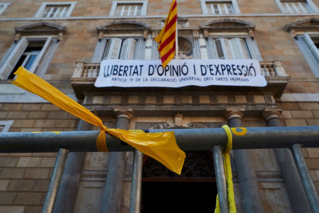 La pancarta situada en el Palau de la Generalitat, con varios lazos amarillos situados en la calle.