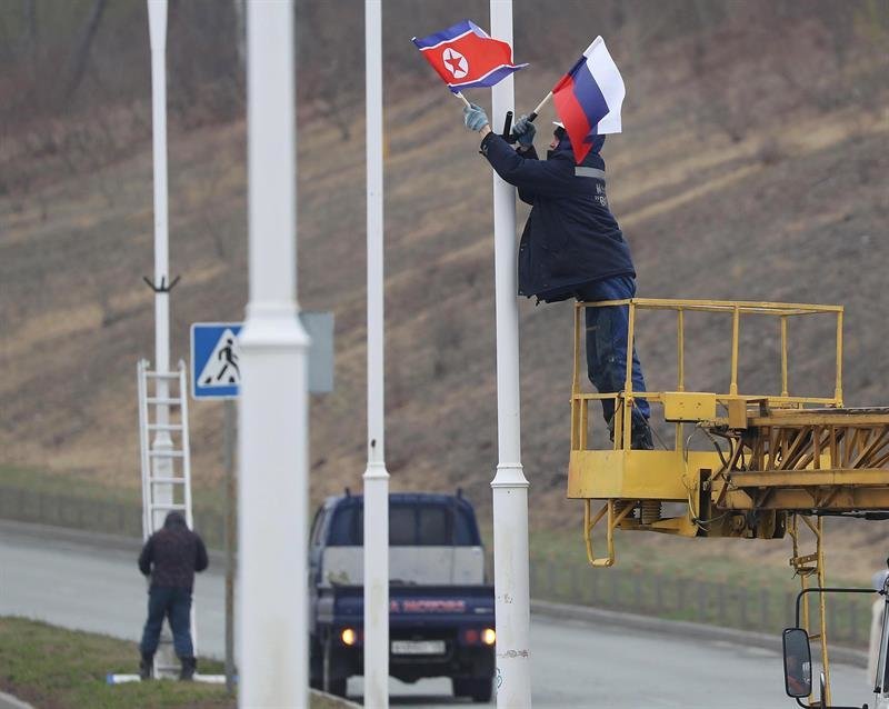 Un empleado coloca sendas banderas de Corea del Norte y de Rusia en las farolas adyacentes a una carretera