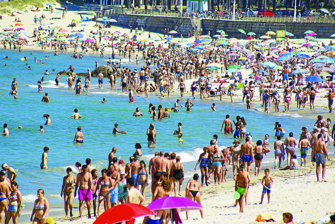 La playa de Samil es la más concurrida de la ciudad. En la fotografía la orilla abarrotada de gente paseando, bañándose y niños jugando en un día de calor de julio.