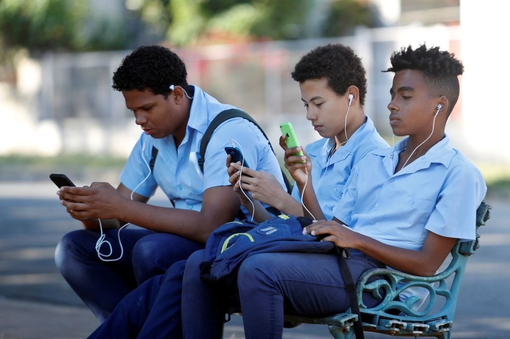 Un grupo de estudiantes cubanos usando su teléfono móvil tras salir de clase.