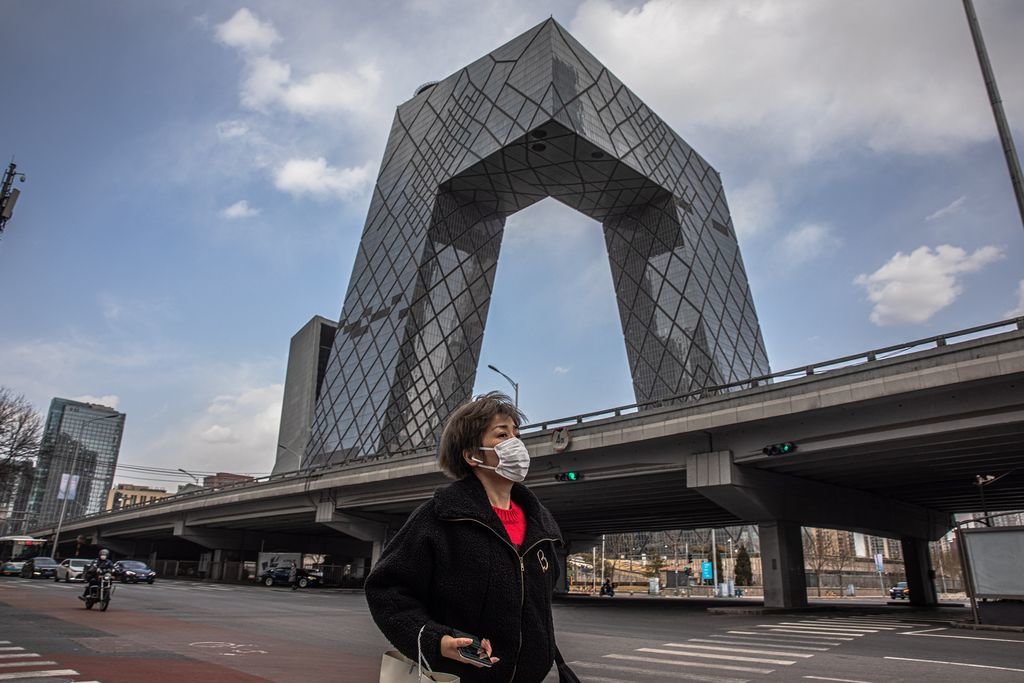 Una mujer protege su cara con una mascarilla mientras pasea por una céntrica calle de Pekín.