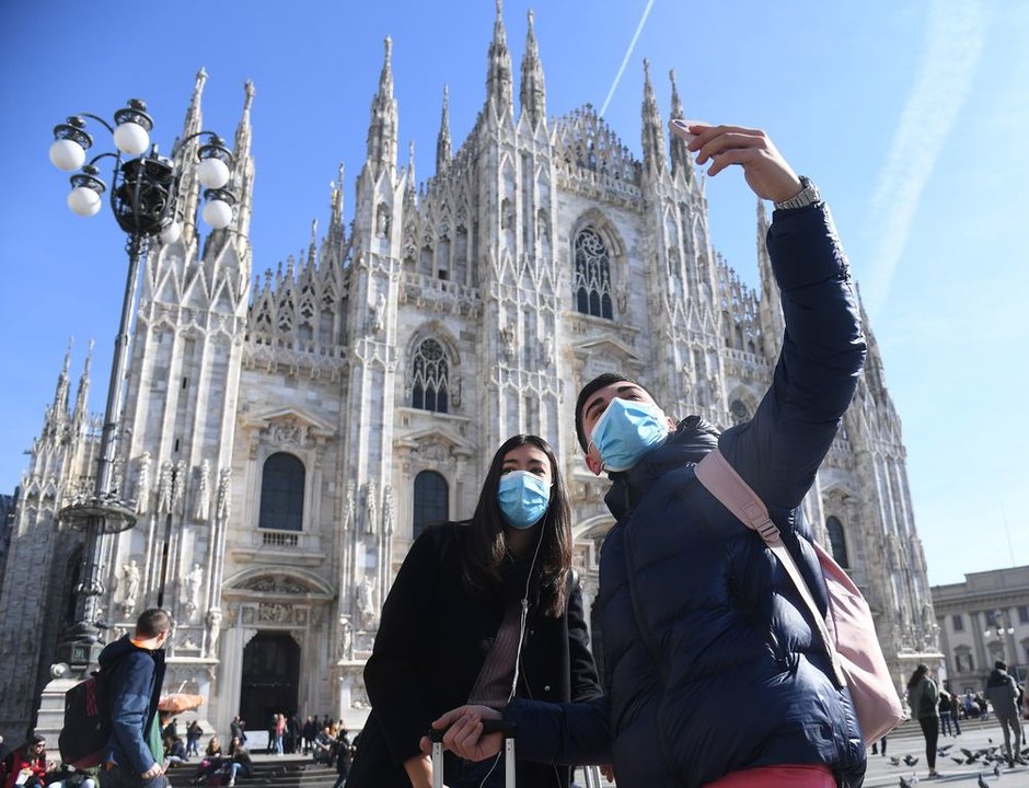 Dos turistas, protegidos con mascarilla, se toman un selfie frente a la catedral de Milán.