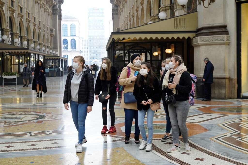 Un grupo de jóvenes turistas se cubren la boca con mascarillas en su recorrido por Milán.