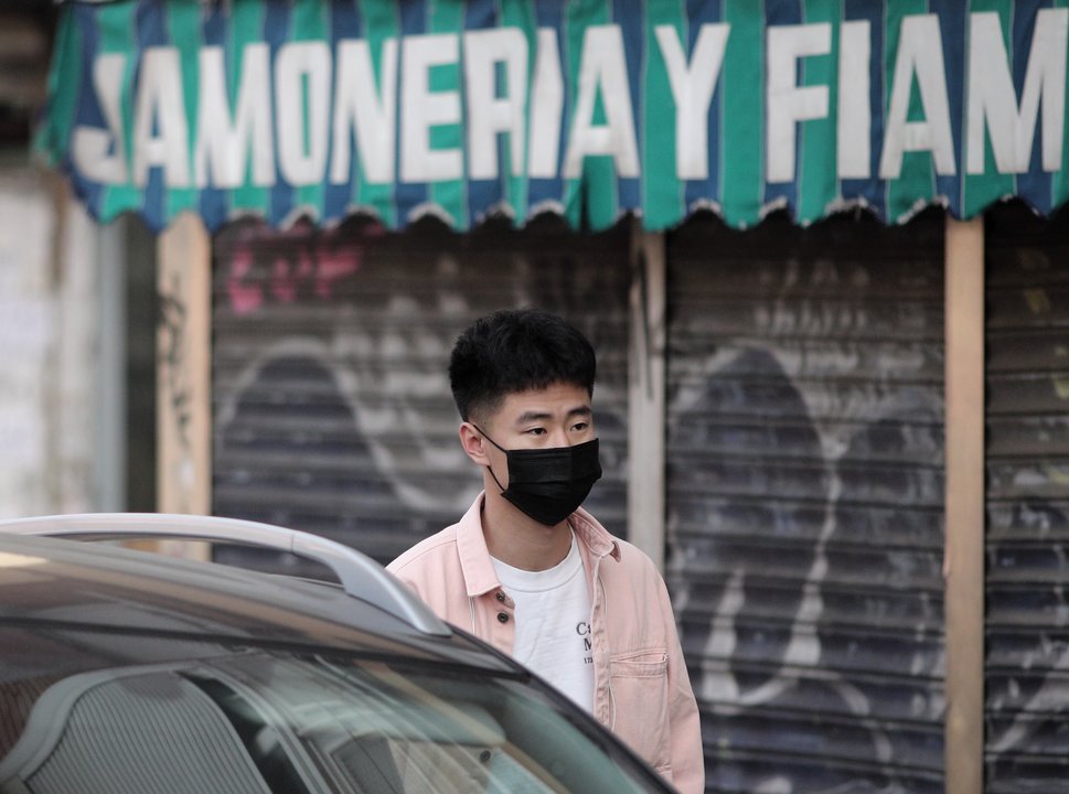 Un joven de rasgos asiáticos camina por el distrito madrileño de Usera protegiendo su rostro con mascarillas