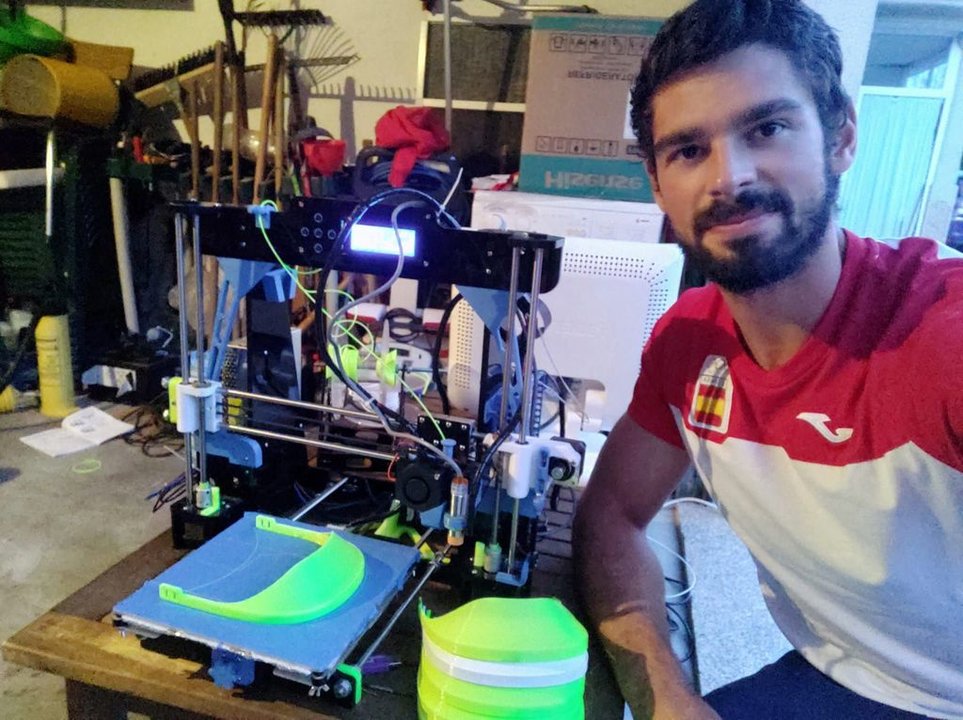 Roi Rodríguez posa junto a su impresora 3D y a la viseras que está elaborando en su casa de Tomiño.