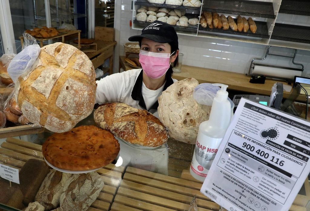 La empleada de una panadería muestra los productos que elabora, al lado información sobre el coronavirus.